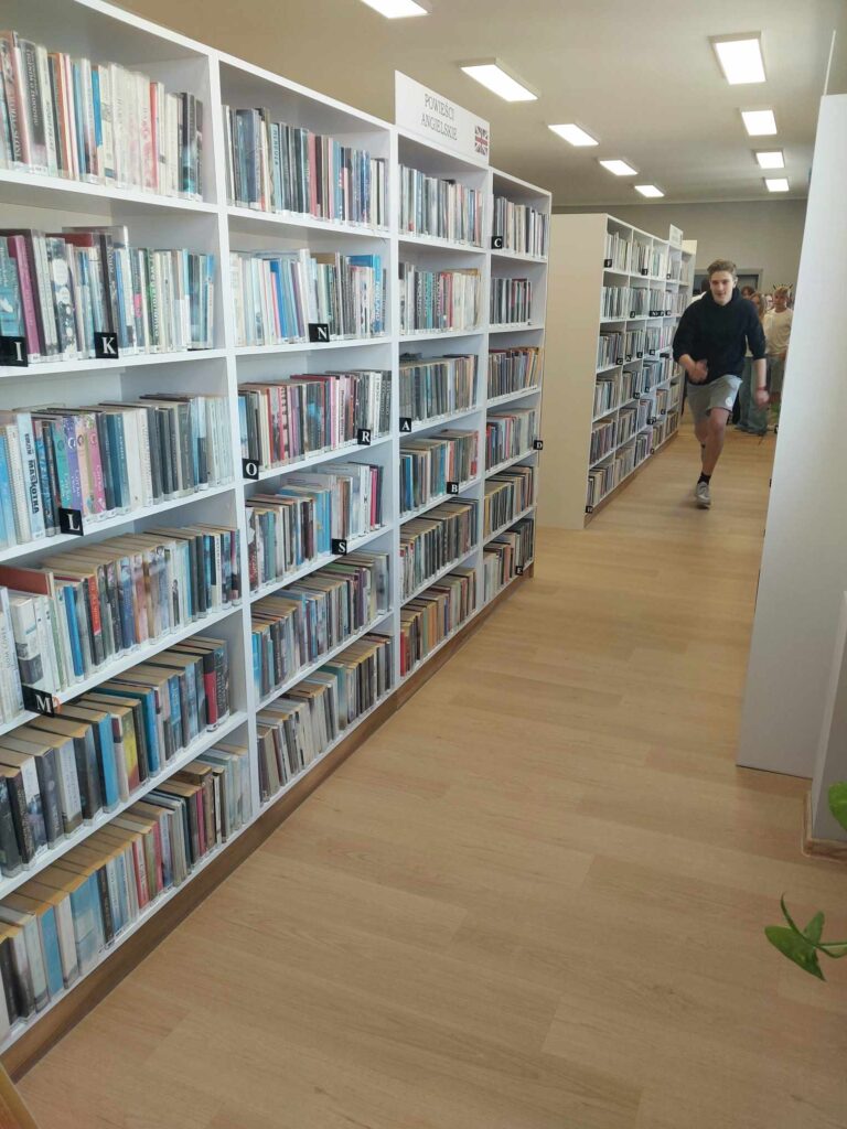 Chłopak biegnie wzdłuż regałów z książkami w bibliotece