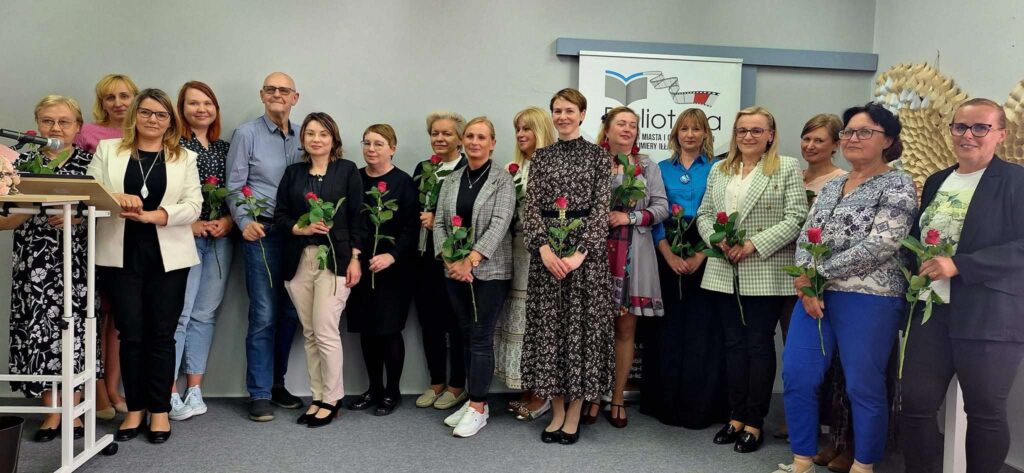 Kilkanaście osób pozuje do zdjęcia trzymając czerwone róże