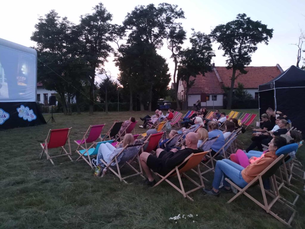 Publiczność widoczna bokiem na leżakach przed ekranem kina plenerowego