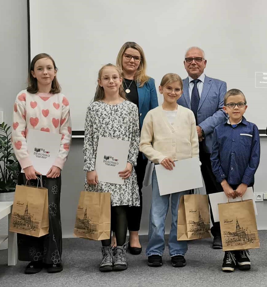 Czworo dzieci z dyplomami i papierowymi torbami w rękach. Za nimi kobieta i mężczyzna.
