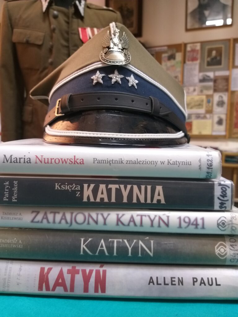 5 książek o katyniu poukładanych w stosik, na nich czapka oficerska
