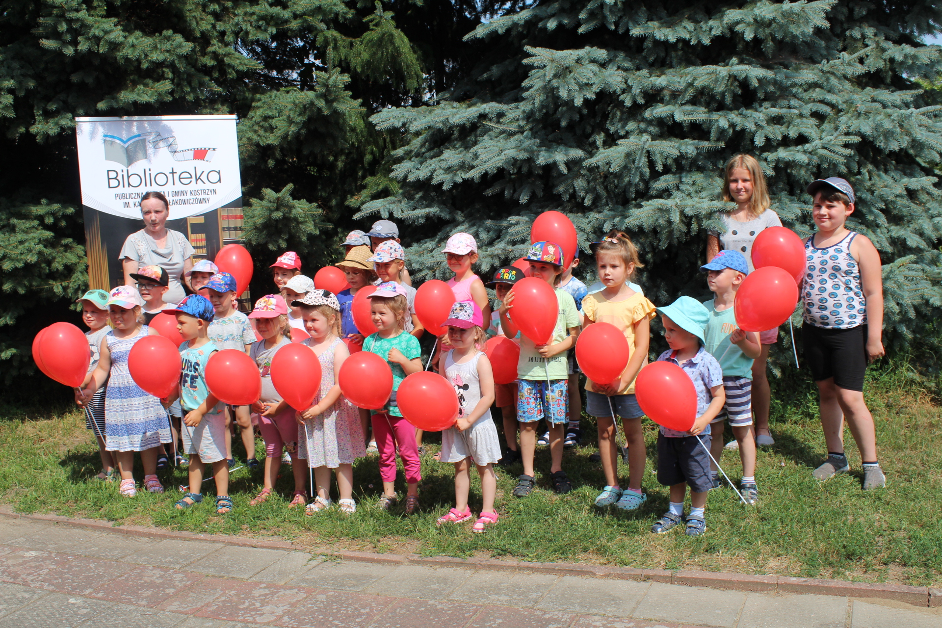 Grupa przedszkolaków z Czerlejna z czerwonymi balonikami w tle rollup biblioteki w Kostrzynie