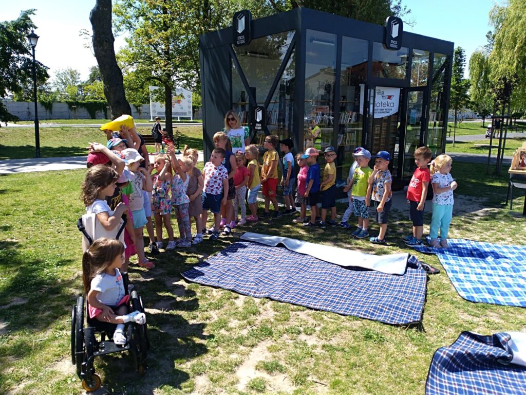 W parku przed Stacją Książki grupa dzieci podczas zabawy .