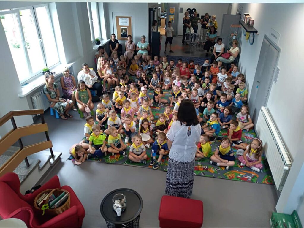 Widok ze schodów na hol biblioteki z dziećmi podczas spotkania literackiego