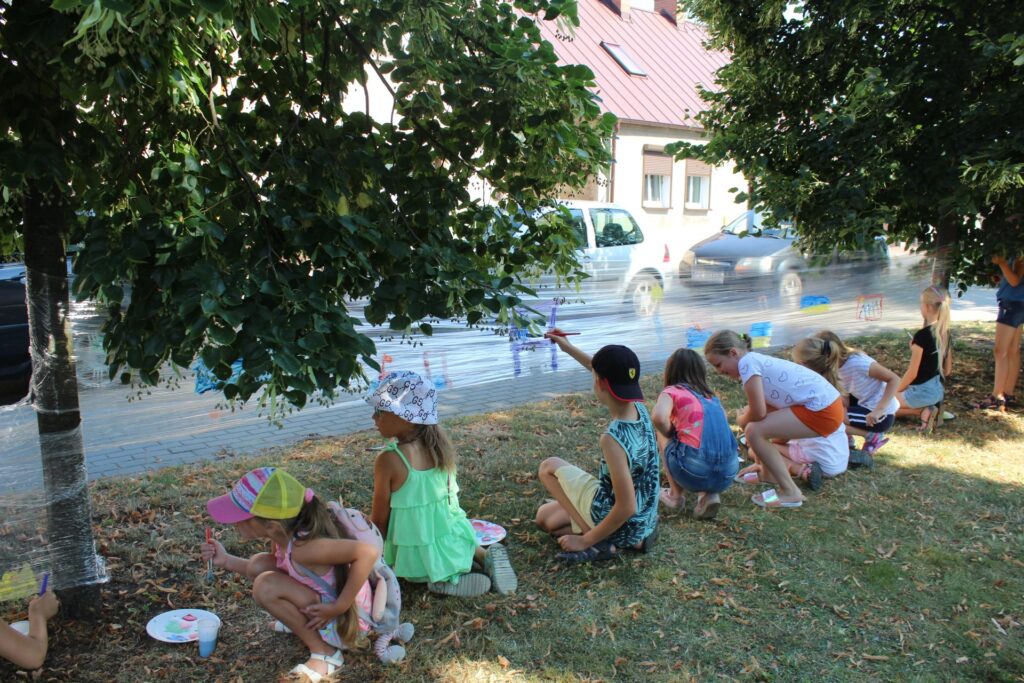 Na rozciągniętej między dwoma drzewami folii dzieci malują farbami.