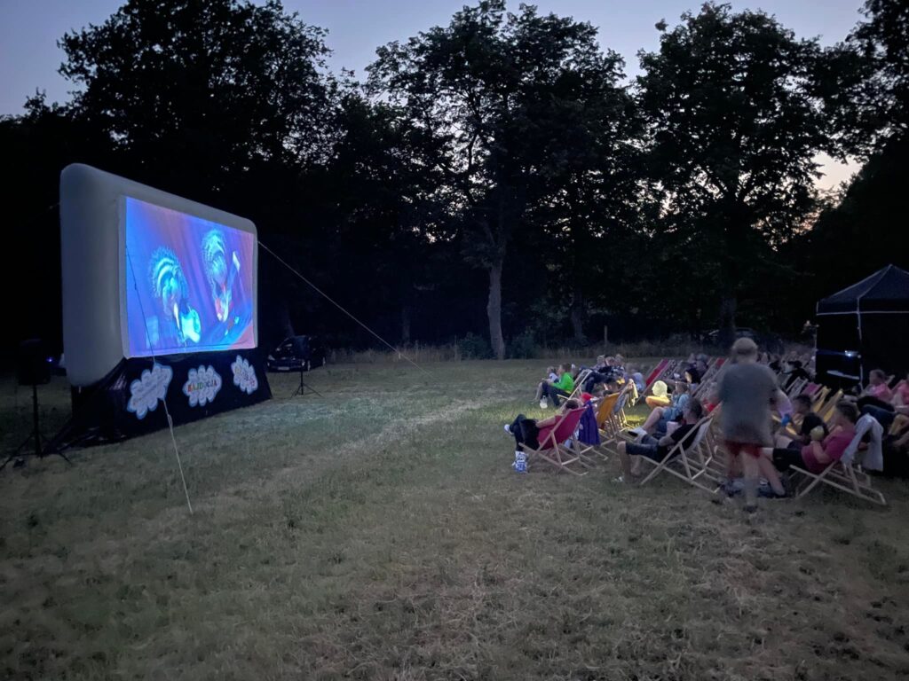 Zmierzcha. Na terenie przy parku ustawiony jest ekran kina plenerowego. Widzowie siedzą na leżakach.