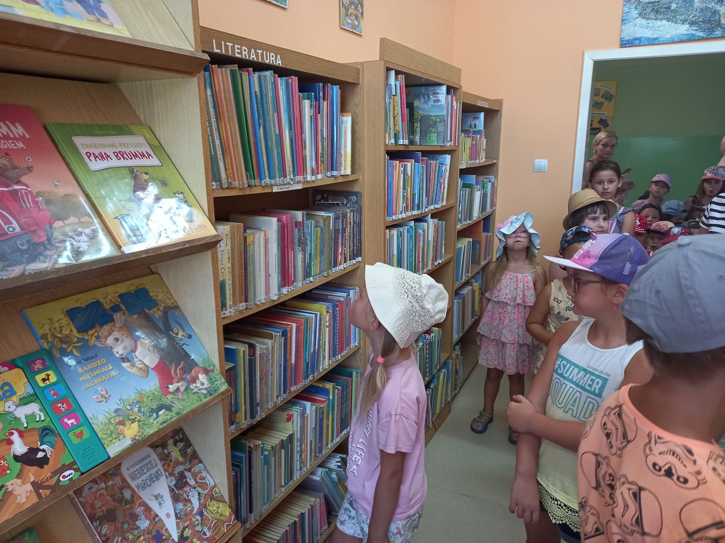 Grupa dzieci w bibliotece wybiera książki z regałów.