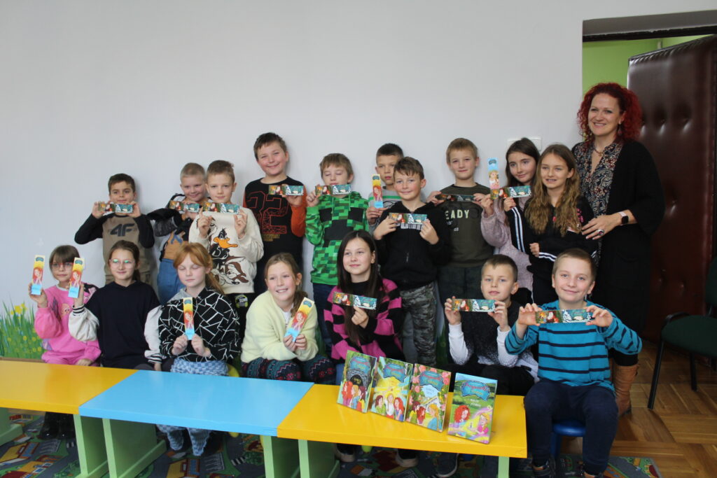 Autorka Jolanta Matuszewska stoi z grupą dzieci trzymających w rękach zakładki do książek.

