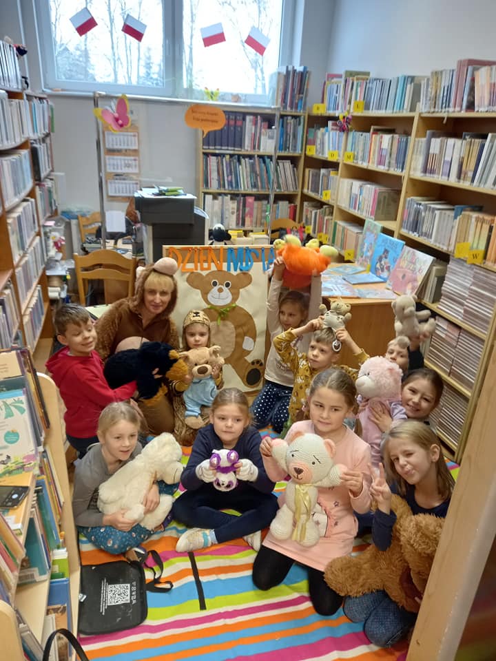 W bibliotece grupa dzieci trzymająca w rękach swoje pluszowe misie. Bibliotekarka w stroju misia.