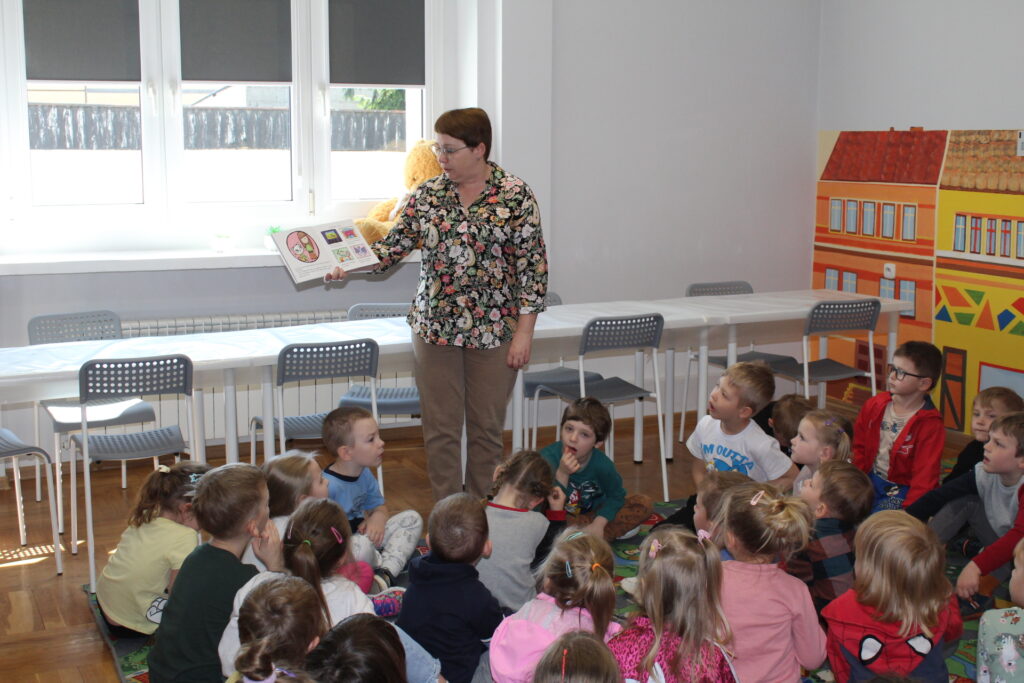 Bibliotekarka pokazuje grupie siedzacych dzieci ilustracje w książce.