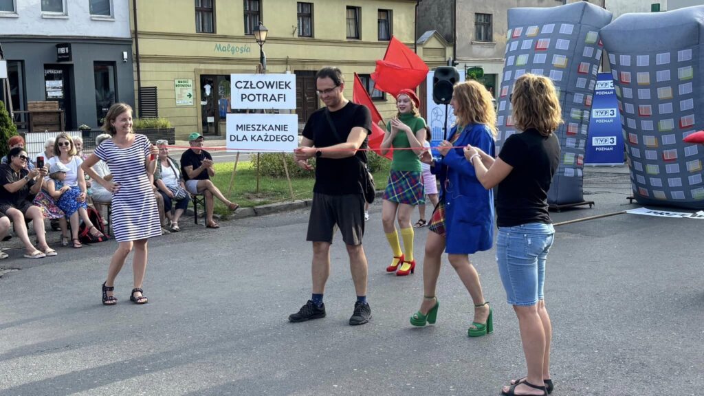 Zdęcie przedstawia aktorów w ubraniach z czasów PRL, występujących na kostrzyńskim Rynku.