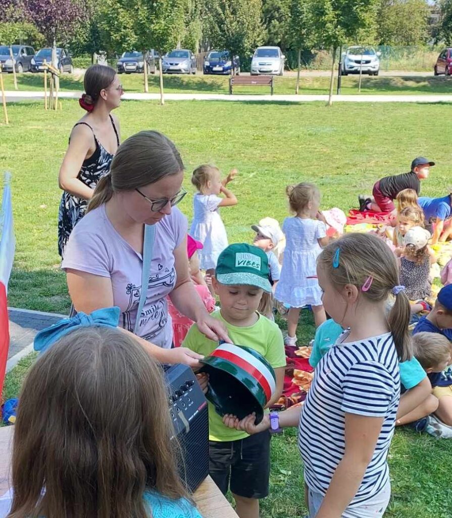 Zdjęcie przedstawia dzieci siedzące w parku przy Stacji Książki podczas Literackiego Czwartku.