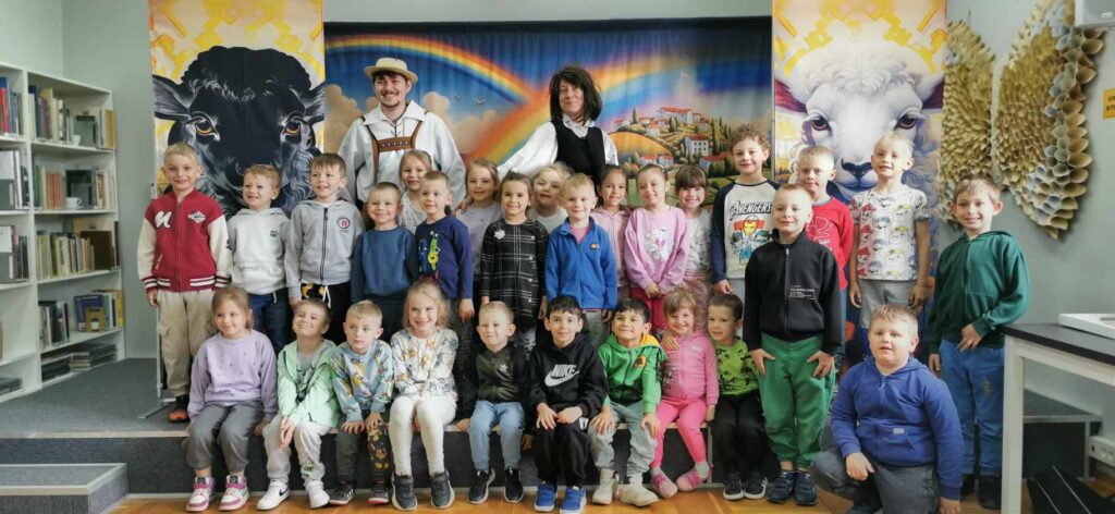 Trzydziestoosobowa grupa dzieci pozuje do zdjecia z aktorami na scenie w bibliotece na scenie