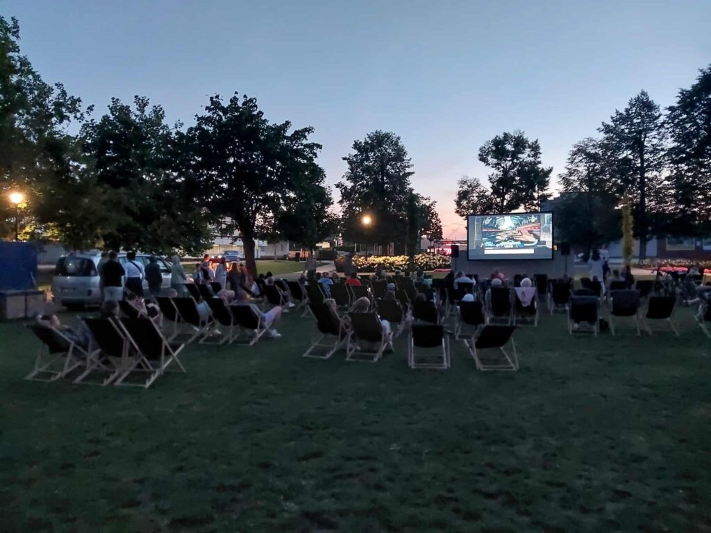 Publiczność tyłem na leżakach przed ekranem kina plenerowego