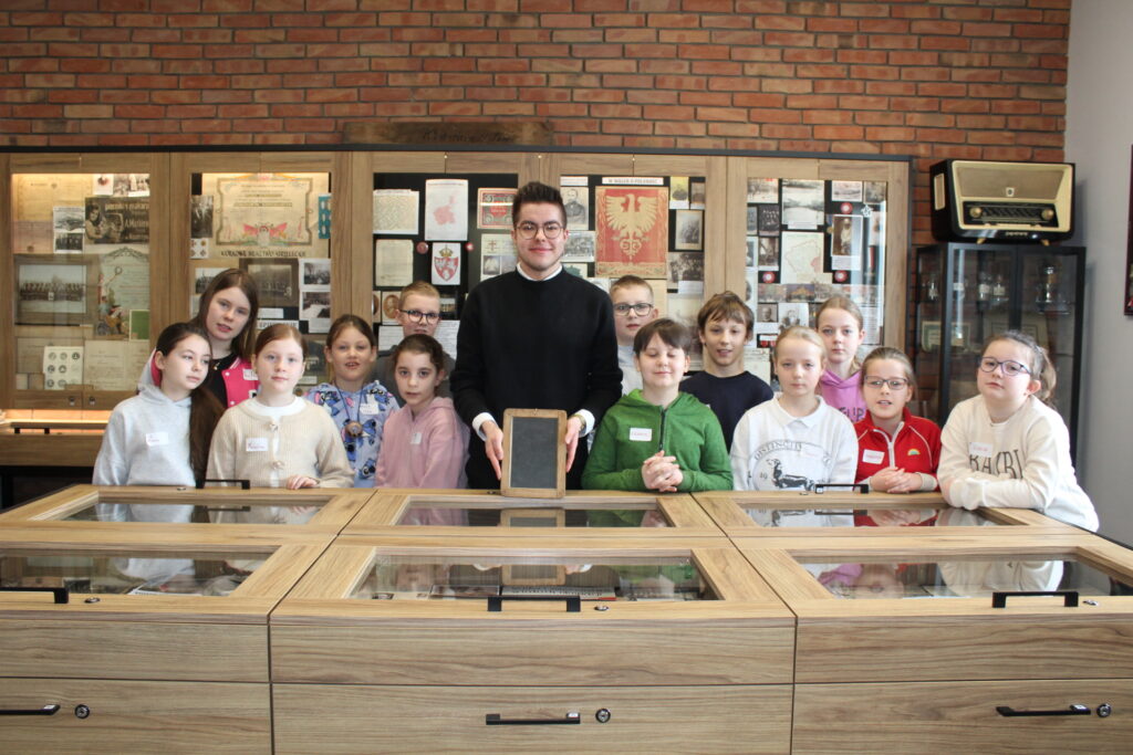 W Izbie Muzealnej przy gablotach stoi grupa dzieci wraz z opiekunem.