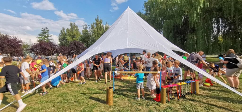 Dzieci pod białym namiotem w parku biorą udział w warsztatach cyrkowych