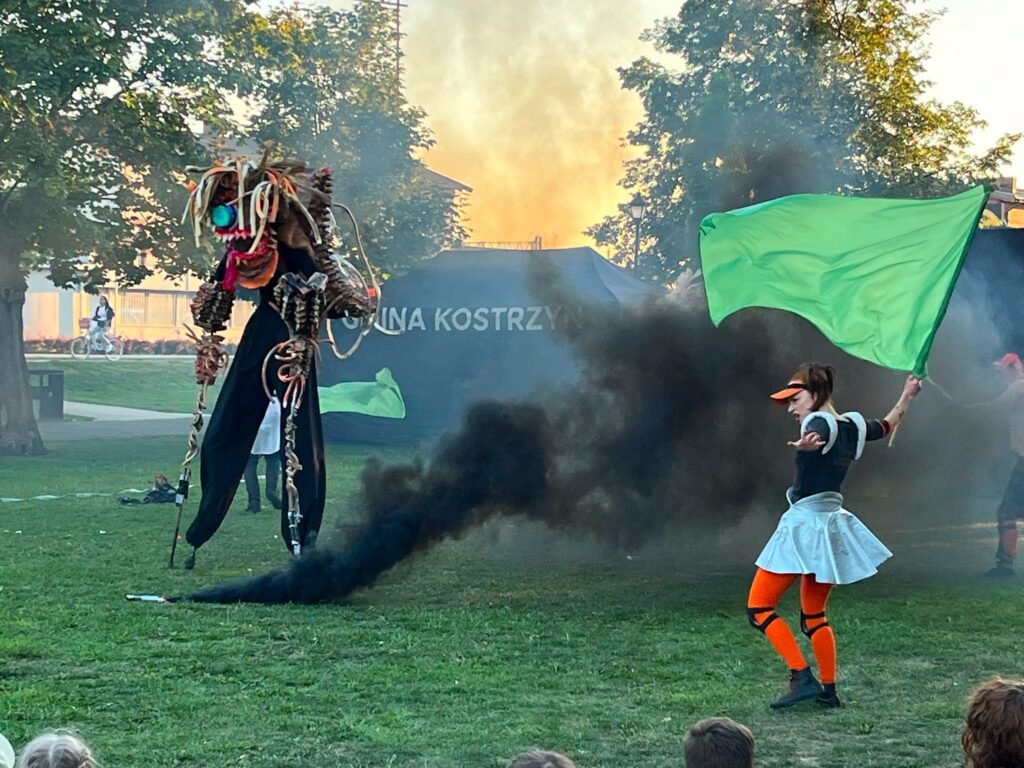 W parku dwoje aktorów, jeden przebrany za potwora. Na środku czarny dym.