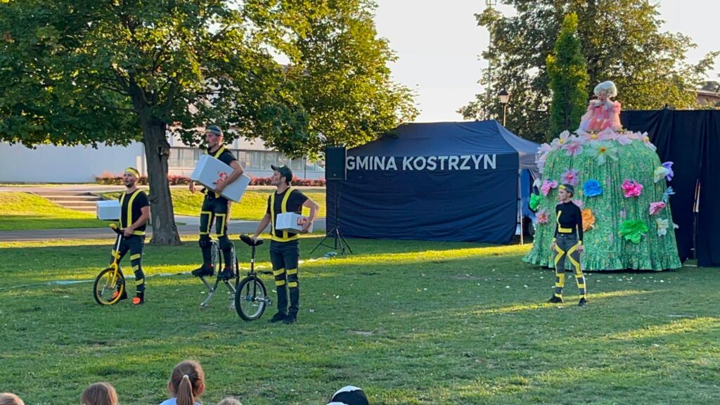 W parku czworo aktorów. Z tyłu niebieski namiot z napisem: Gmina Kostrzyn.