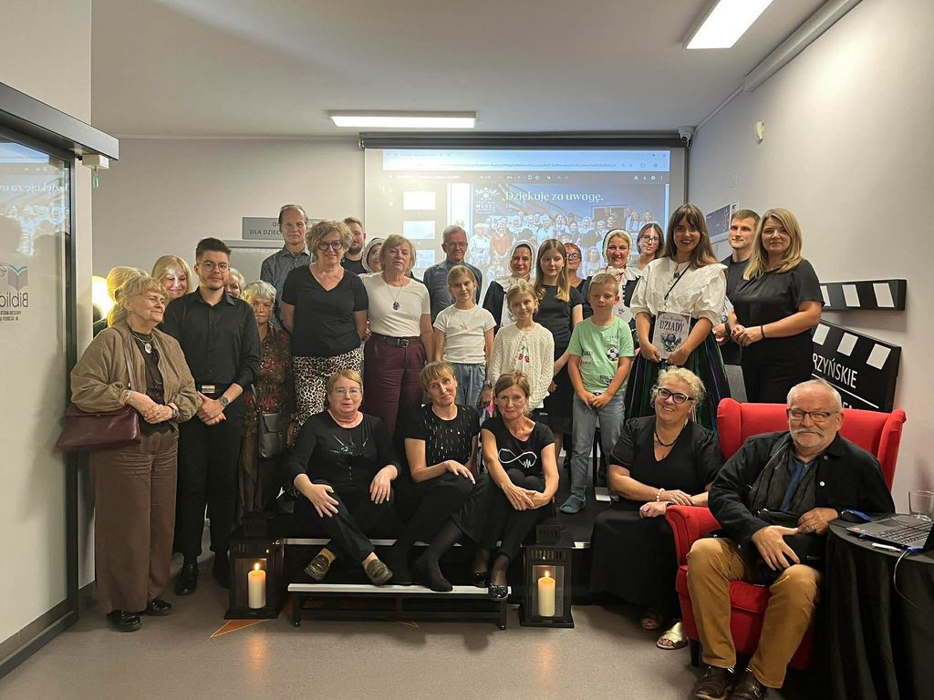 Około 30 osób pozujących do zdjęcia grupowego po Narodowym Czytaniu stojących i siedzących na scenie w holu biblioteki