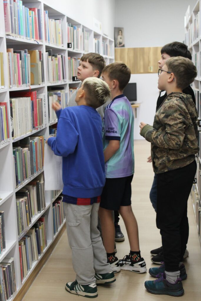 Kilkoro ucznuiów szuka książki na regale bibliotecznym.
